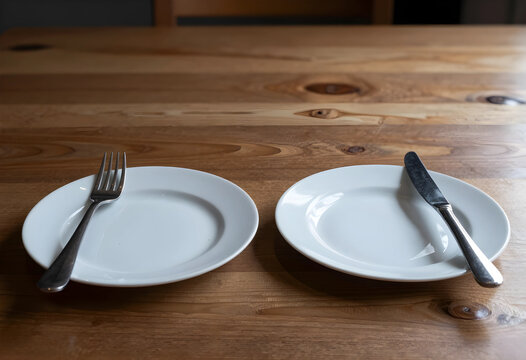 Food insecurity and hunger crisis, empty plates with cutlery on a wooden table, poverty and economic hardship