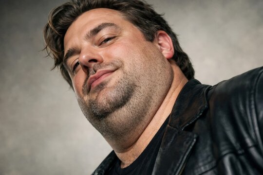 Low angle portrait of confident heavyset man in black leather jacket, casual lifestyle and character headshot concept.