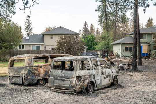 Spokane, Washington, United States - 14 August 2026: View of two burnt-out vehicle shells in a residential yard, with scorched ground and intact houses standing in the background.