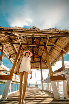 Woman tourist stay on balcony of the hut lap into the sea, relax moment on wooden pier, enjoy sunset of the summer trip in tropical island