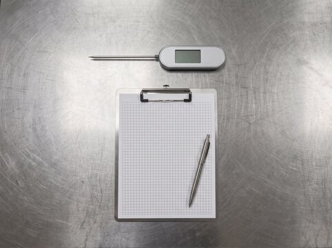 Digital thermometer clipboard and pen on stainless steel surface