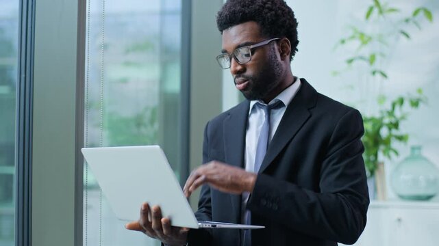 Thoughtful African American business man typing laptop thinking experienced businessman work with computer male guy executive working think online difficulties decision in office looking near window