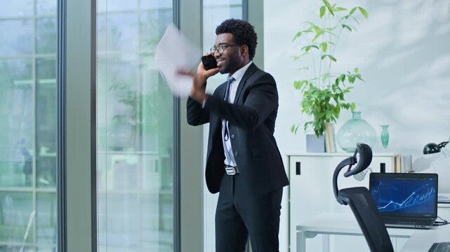 Stressed angry African American business man arguing yelling with mobile phone and papers in office ethnic mad aggressive businessman male guy yell argue talking smartphone discuss documents mistake