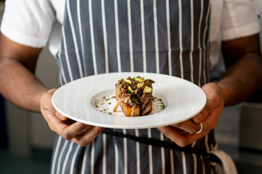Chef Showcasing a Beautifully Plated Gourmet Dish at a Bustling Restaurant Kitchen
