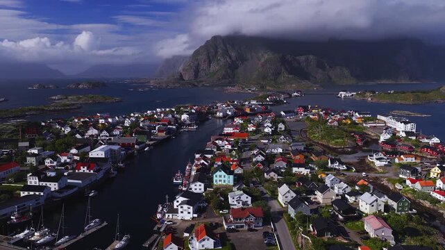 An aerial view captures the coastal village of Henningsvaer in Lofoten, Norway, showing traditional houses, harbour channels, boats, and mountain peaks.