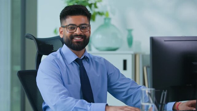 Happy Muslim business man Arabian male typing computer smiling looking at camera in office worker Indian businessman male productive executive specialist working with desktop work smile satisfied