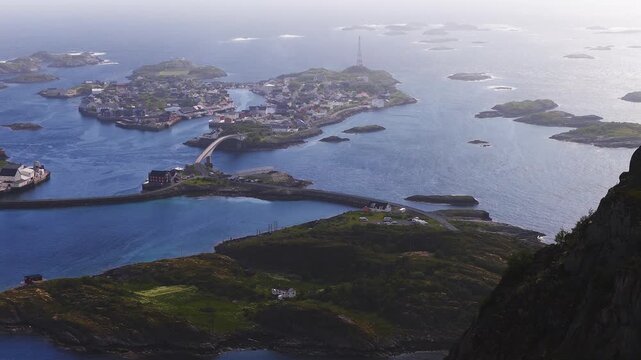 An aerial panorama shows the coastal village of Henningsvaer, its bridges connecting rocky islets, and surrounding Norwegian sea waters in Lofoten, Norway.