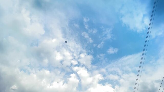 Small airplane flying high in blue sky with white fluffy clouds and power lines on side. travel, aviation, nature, background, summer