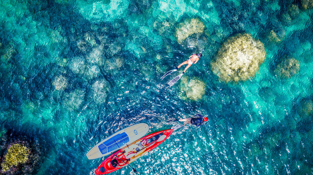 Top aerial view of Group of tourist are enjoy on water sport paddle sup-board with kayaking along at the edge of the sea beach under crystal clear of water in the island of summer trip