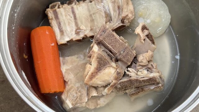 Boiled meat bones with whole carrot and onion in metal pot, making broth or pet food. cooking, soup, ingredients, homemade, dog food
