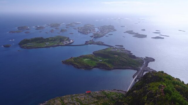 An aerial perspective shows the rocky islands and connecting bridges leading toward the fishing village of Henningsvaer in Lofoten, Norway on a bright day.