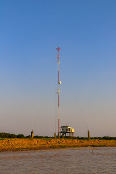 Kampong Phluk, Siem Reap Province, Cambodia - 05 February 2020: View of a tall communication tower standing on the muddy banks of the Tonle Sap lake under a clear blue sky.
