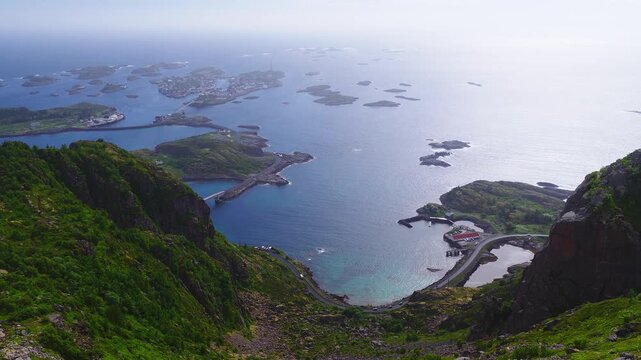 An aerial panorama captures the archipelago of Henningsvaer in Lofoten Norway, surrounded by sea water, coastal roads, bridges, and rugged rocky mountains.