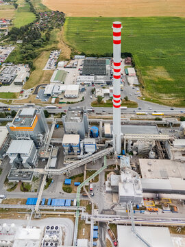 Aerial view of the Mondi SCP factory featuring a tall red and white striped chimney, industrial buildings, and pipelines surrounded by green fields in Ruzomberok, Zilinsky kraj, Slovakia.