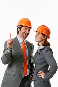 L&auml;chelndes Business-Paar mit orangen Bauhelmen, Daumen hoch, wei&szlig;er Hintergrund, Konzept f&uuml;r Architektur und Bauwesen.