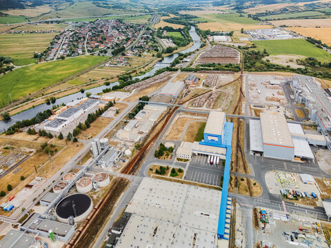 Aerial view of the Mondi SCP factory complex with industrial buildings, storage areas, and railway tracks near the Vah river and green fields in Ruzomberok, Zilinsky kraj, Slovakia.