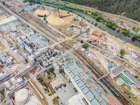 Aerial view of the Mondi SCP factory complex featuring large wood chip piles, industrial buildings, storage tanks, and railway tracks alongside a river in Ruzomberok, Zilinsky kraj, Slovakia.