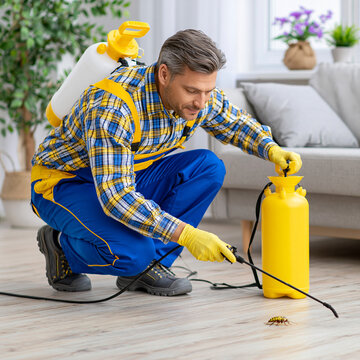 Pest control worker in protective uniform applying chemical spray indoors with chemical