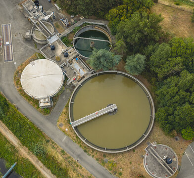 Aerial view of circular settling tanks and clarifiers at a wastewater treatment plant, showing industrial water purification infrastructure in Portes-les-Valence, Auvergne-Rhone-Alpes, France.