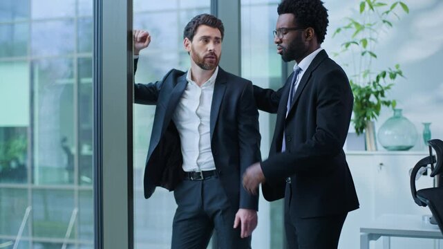 Two multiethnic business men talking about problem African American worker help supporting Caucasian upset businessman looking at window suffering businessmen males talk about work trouble in office