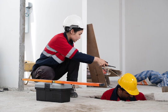 Construction engineer directing underground utility work with a radio during indoor building renovation. Site inspection, workplace safety, engineering supervision, project coordination and teamwork.