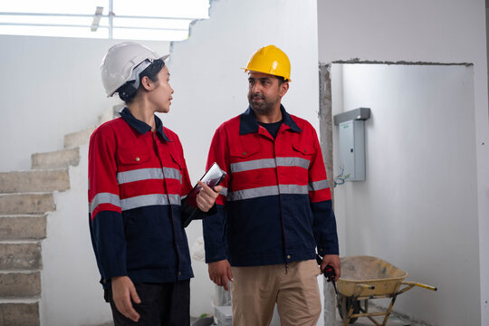 Construction engineers discussing project progress inside an unfinished building while reviewing site conditions with a digital tablet. Teamwork, building inspection, renovation, project management.