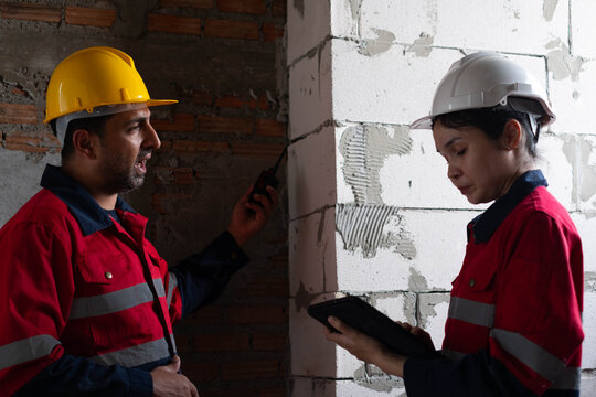 Construction engineers reviewing inspection records at an unfinished building, using digital devices to monitor structural quality, safety compliance, and project progress for residential construction