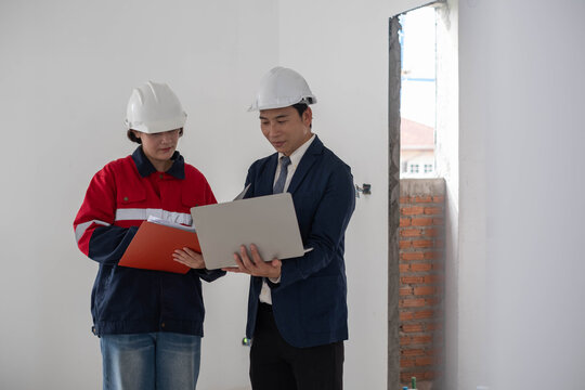 Construction professionals use a laptop and review project documents inside an unfinished building, representing engineering, teamwork, digital planning, architecture, supervision, project management.