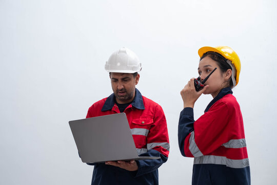 Construction workers in hard hats use a laptop and radio at a worksite, showing field communication, project coordination, engineering, workplace safety, digital technology, and industrial operations.