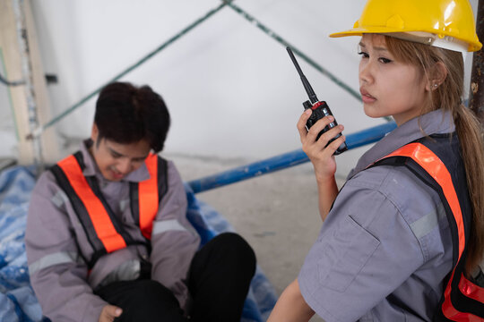 Construction supervisor using a radio to report a workplace injury while an injured worker rests at a jobsite, emergency communication, safety, accident response, teamwork, and worker protection.