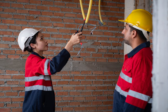 Electrical engineers inspecting ceiling wiring during residential construction, wearing safety helmets, protective, showcasing teamwork, electrical installation, workplace safety, building renovation.