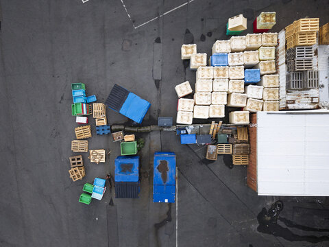 Aerial view of industrial logistics area with stacked wooden pallets, blue plastic containers, and shipping crates on asphalt ground in Gothenburg, Vastra Gotaland Count, Sweden.