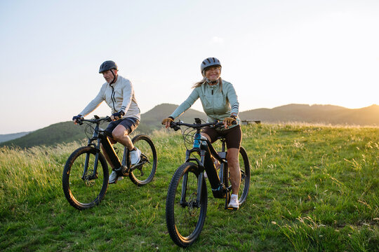 Happy mature couple riding e-bikes through scenic countryside.