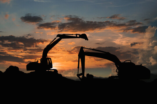 Two Crawler excavators silhouette are digging the soil in the construction site on   sunset clouds  sky background .