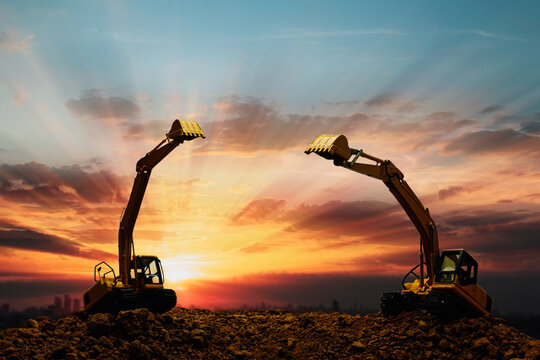 Two Crawler excavators  are digging the soil in the construction site on   sunset clouds  sky background .
