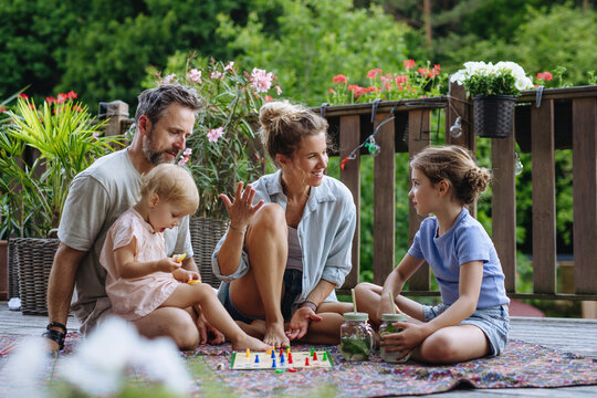 Family enjoying board game together on outdoor terrace during summer.