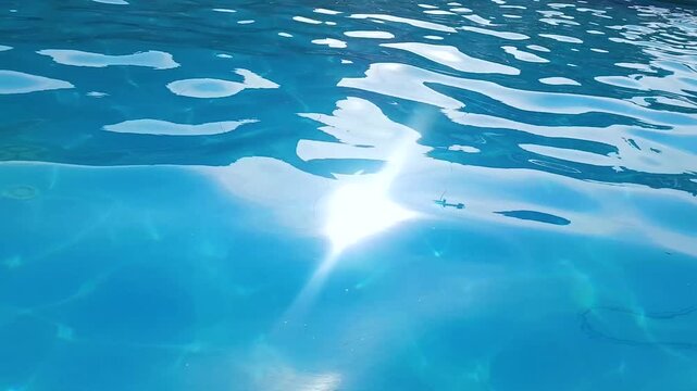 Close up of water caustics in deep blue swimming pool, gentle ripples with glinting sunlight reflections, clear azure water motion in outdoor pool, relaxing summer resort background, slow motion