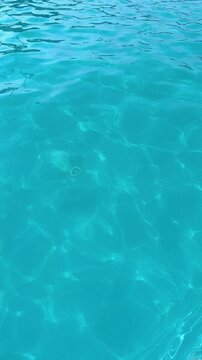 Close up of water caustics in bright blue swimming pool, vertical frame, rippling surface with glinting sunlight reflections, clear turquoise water motion in outdoor pool, relaxing summer vacation