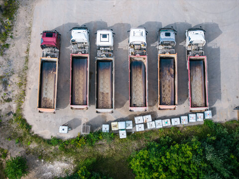 Aerial view of a row of empty dump trucks parked in a gravel lot, representing industrial logistics and construction material transport, Mundigciems, Talsi Municipality, Latvia.