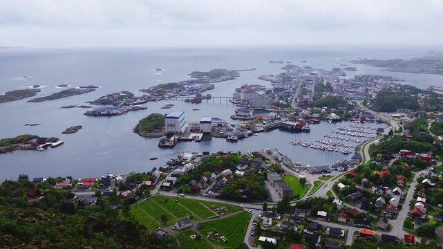 An aerial wide panorama of Svolvaer port, harbor, houses, and surrounding islands on a cloudy daylight afternoon in Lofoten, Norway.
