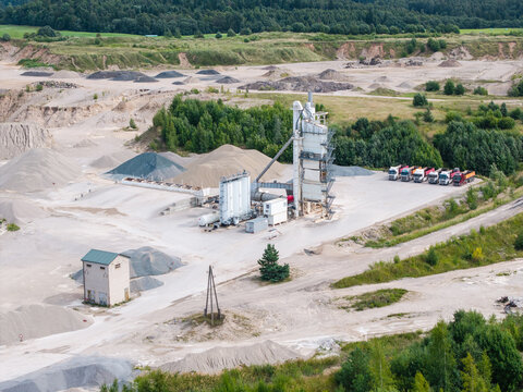 Aerial view of a concrete production facility with industrial silos, piles of gravel and sand, and a fleet of trucks parked on-site in Mundigciems, Talsi Municipality, Latvia.