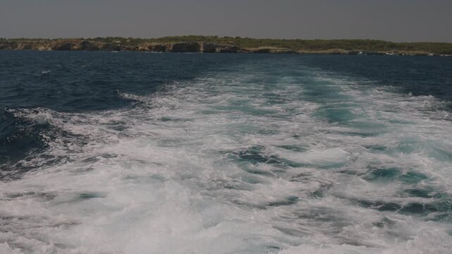 Boat wake foam trail with coastline in the distance