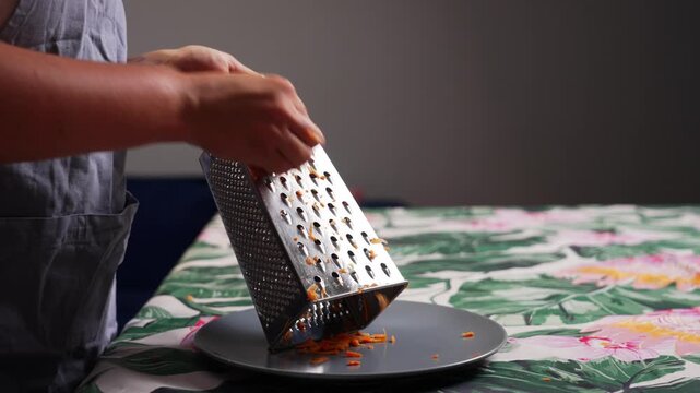 Fresh carrot being grated with hand grater in kitchen during homemade meal preparation using healthy vegetables for everyday cooking. High quality 4k footage