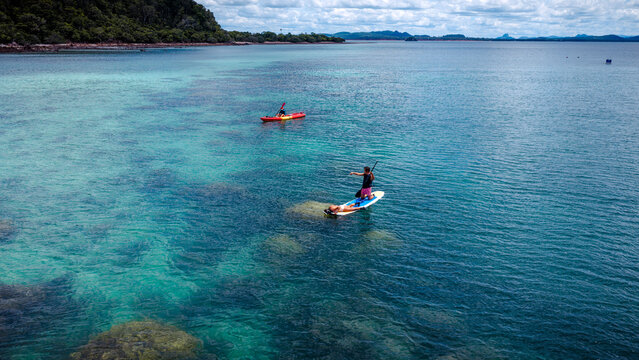 Top aerial view of Group of tourist are enjoy on water sport paddle sup-board with kayaking along at the edge of the sea beach under crystal clear of water in the island of summer trip