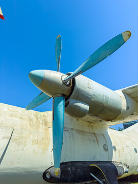 Old airplane propeller stands under blue sky at an outdoor display near a museum in mid-afternoon sunlight