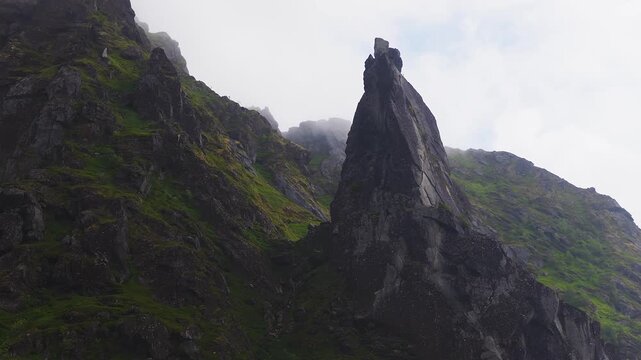 An aerial view shows the sharp rock spire of Svolvaergeita rising against rugged mountain slopes with mist in Lofoten, Norway.