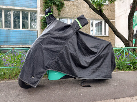 Black nylon motorcycle cover securely fitted over a parked motorbike in a residential courtyard beside a multi story building ensuring long term protection and cleanliness