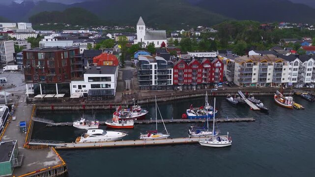 Aerial view of moored boats, yachts, and coastal architecture along the harbor waterfront in Svolvaer, Lofoten, Norway on an overcast day.