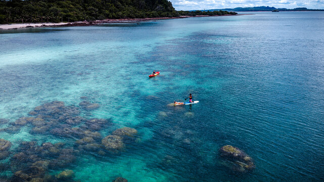 Top aerial view of Group of tourist are enjoy on water sport paddle sup-board with kayaking along at the edge of the sea beach under crystal clear of water in the island of summer trip