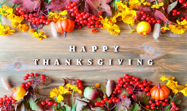 Thanksgiving background. Festive autumn border with Happy Thanksgiving wooden letters text, berries, pumpkins, apples and flowers on the wooden surface
